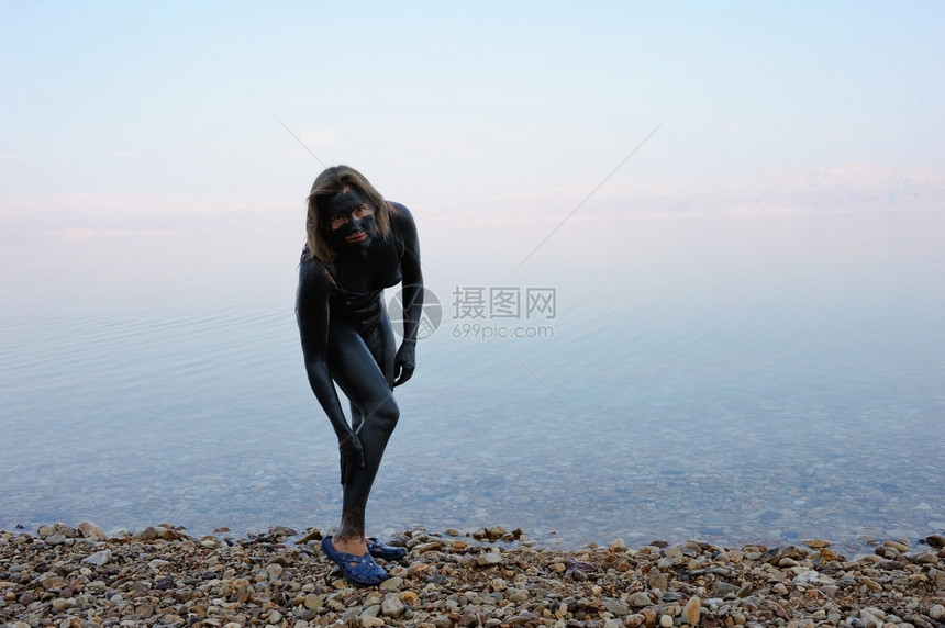 早晨女人在死海的岸边沾上治疗泥巴天空女士图片