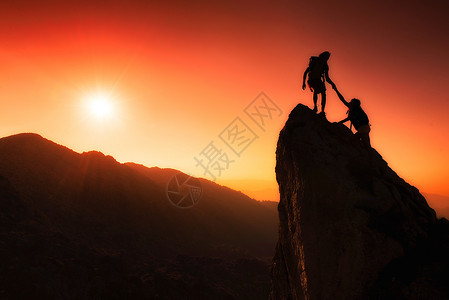 一种登山者团队帮助高峰会在日落时一个奇妙的山地风景中携手合作目标岩石图片