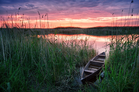 芦苇景日落时在湖边的木船夕阳时在湖边的休养和自由概念月光之景黄昏时在湖边的木船奇幻天空下的单身银行水背景