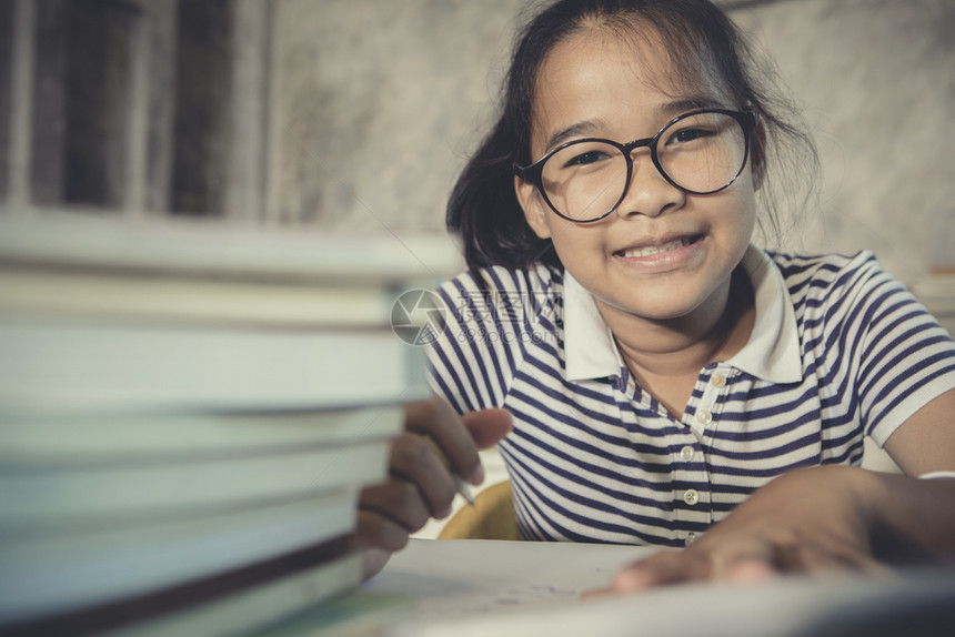 学生身戴眼镜的亚裔青少年在家庭工作时带着堆叠的学校书前台正在做女士图片
