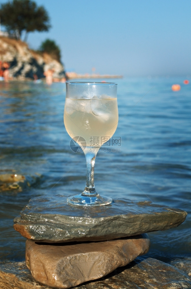 太阳海浪冲刷的岩石边杯白葡萄酒被海浪冲洗过休息滩图片