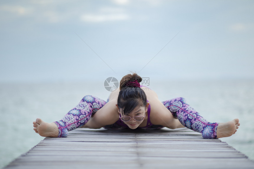 美丽的女人在海木码头做瑜伽在海龟上摆姿势假期海滩活动图片