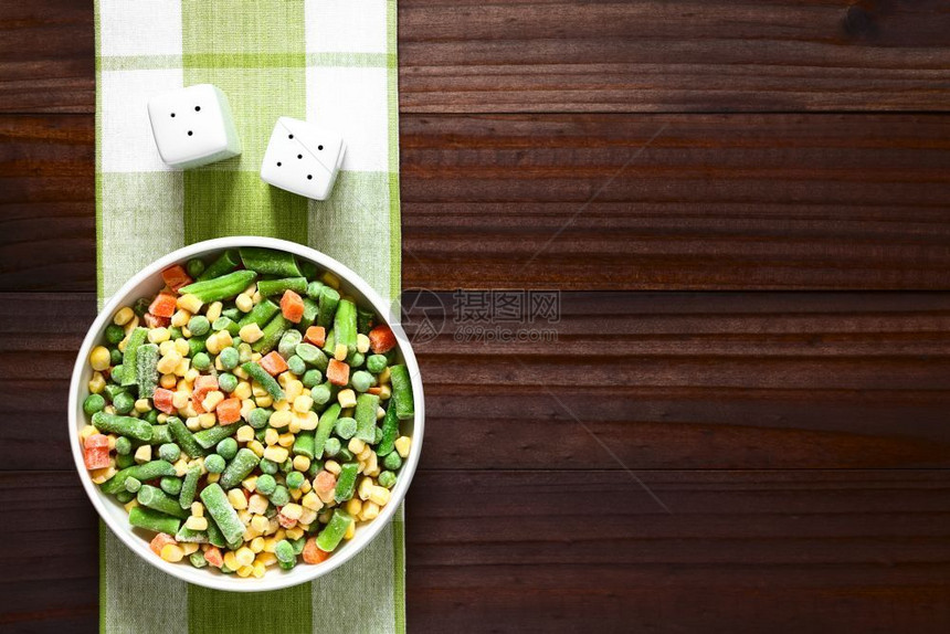 生的水平冷冻混合蔬菜绿色豆梨胡萝卜甜玉米在碗里用天然光冰冻混合蔬菜拍摄黑木上方图片