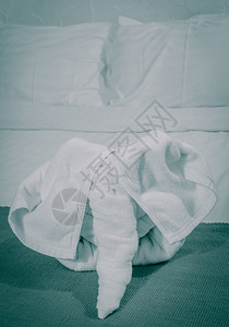 假期折叠白毛巾大象形状的白毛巾在色床上用泰国风格的旅馆卧室家具图片