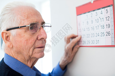 辅助八十年代痴呆的老者看着墙壁日历活的图片
