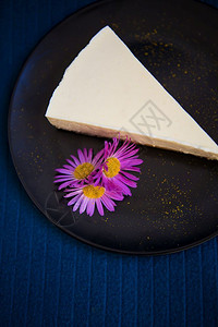 奶油紫米糕甜点食物披着紫花的奶油乳酪蛋糕涂在黑色盘子上的紫花朵涂在黑色盘子上的紫花朵乳制品背景