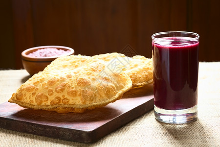 玉米低聚肽典型的玻利维亚传统小吃叫做派斯特尔深炸糕点和盛满奶酪的糕点配有木板上的紫玉米饮料Api木板上的紫玉米饮料用自然光拍攝选择焦点聚在背景
