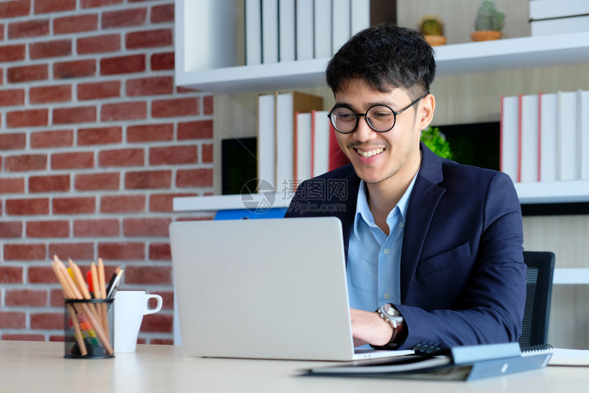 报告人们年轻亚洲商在办公室使用笔记本电脑时微笑商业办公室的生活方式概念在办公用笔记本电脑工作时笑信息图片
