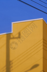 黄色建筑墙壁表面电杆的阴影垂直框中与蓝色天空对立的电线水泥框架的图片