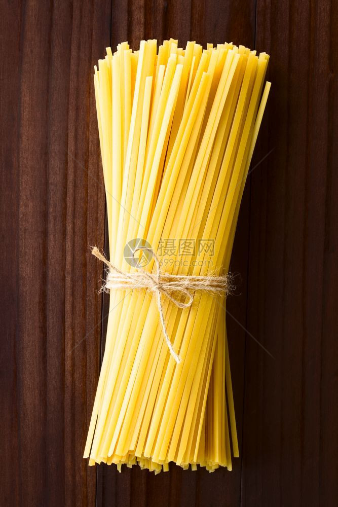 意大利语高架黄色的生扁长丝带意大利面叫做Fettuccini绑成一捆在深色木头上拍下RawFettucciniPasta图片