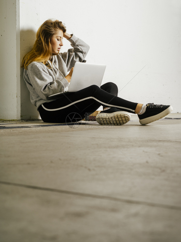 在职的门厅头发一名年轻女学生坐在走廊上手持笔记本电脑手机及书籍图片