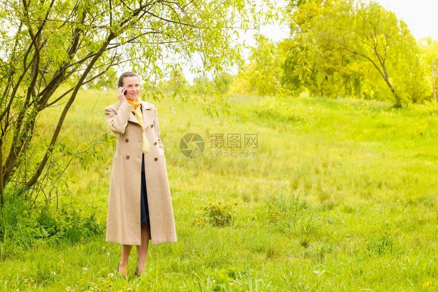 请讲柳一位优雅的高级女商人穿着大衣和黄色围巾在春日下用手机公园打电话下面图片