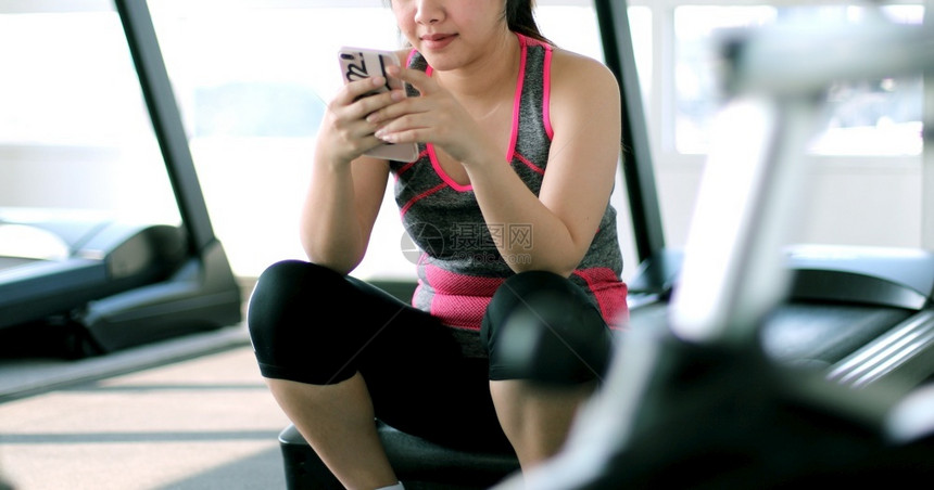 胖的移动微笑在健身房使用移动电话的年轻亚洲妇女图片