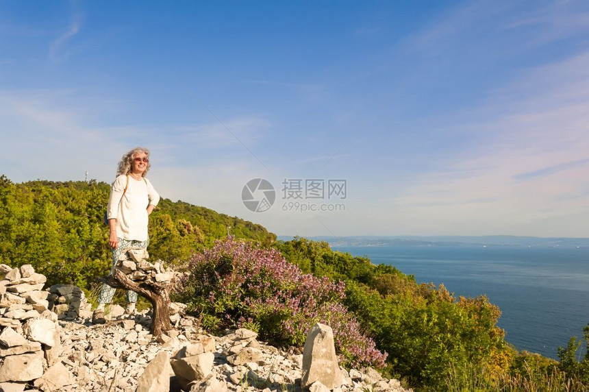 户外阳光照射大约60岁的女在悬崖上徒步旅行享受阳光的海景健康生活习惯假期图片