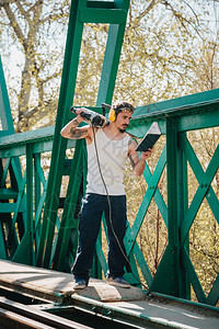 阴影年轻建筑工人在读一本关于旧钢铁路桥的书肩上用液压锤子敲着在职的天图片