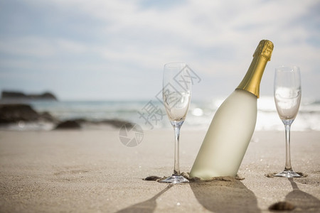 海岸娱乐热带滩的香槟瓶和沙上的两杯香槟酒瓶和沙滩上的两杯喝图片