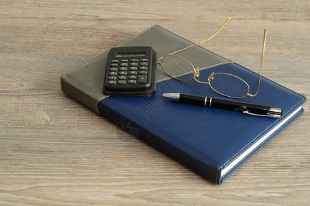 书在木制背景上展示的笔记本顶上计算器笔和阅读眼镜成功商业图片