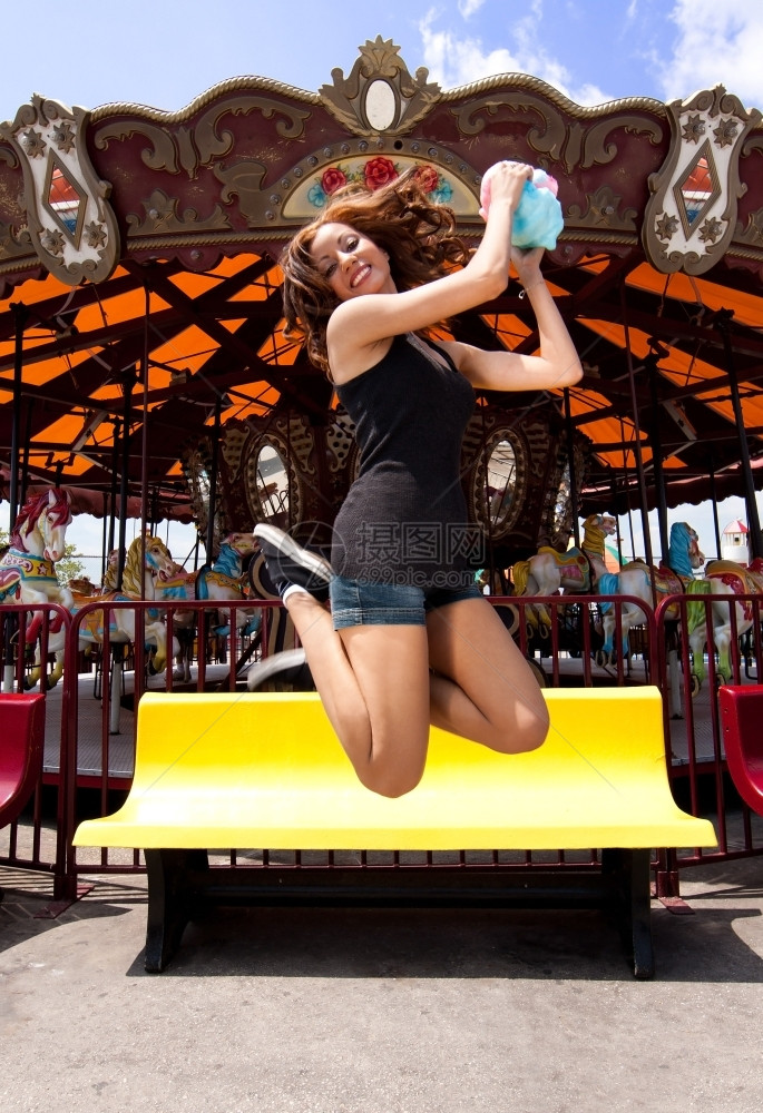 保持美丽的快乐女孩在梅里面前跳起喜悦的快乐女孩在科尼岛嘉年华狂欢节主题游乐园骑着棉花糖快乐的跳跃图片