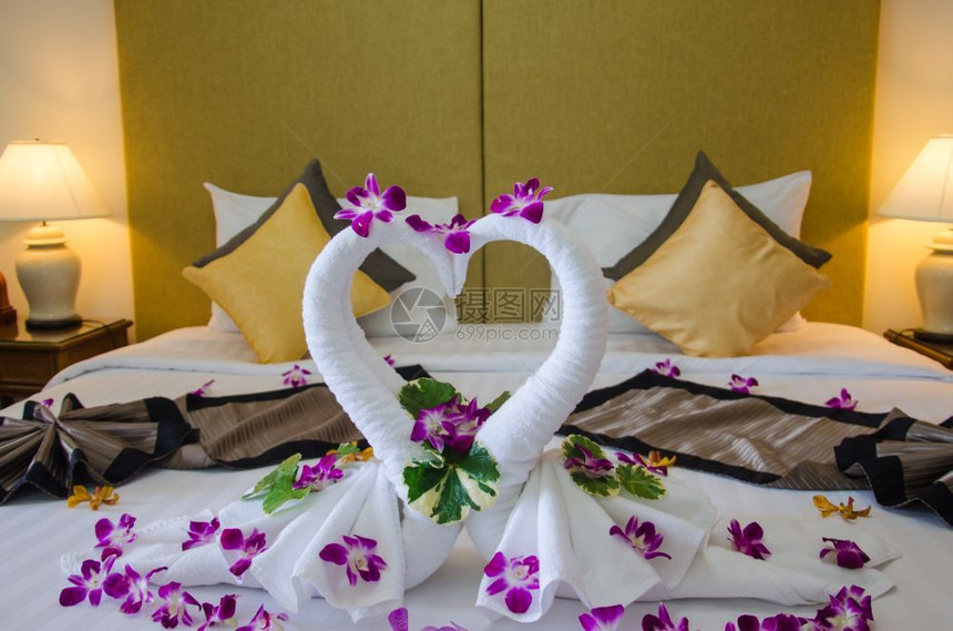 自然室内卧天鹅毛巾和床上的兰花酒店房间对夫妇来说是浪漫的奢华枕头图片