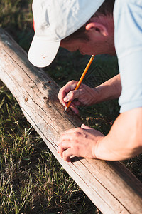 帽子白色的男在花园工作时测量木材后用铅笔打标记木头图片