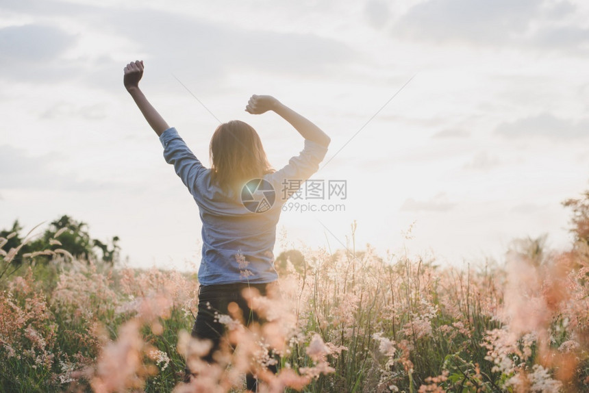 黄色的年轻美丽女士站在草原上举起双臂在空中露出青草地日落时与大自然相享受户外金的图片