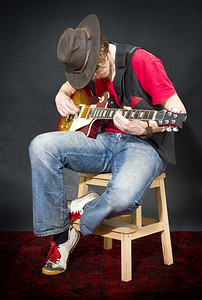 一个戴着旧皮帽的音乐家坐在凳子上弹吉他小地毯乐器的图片