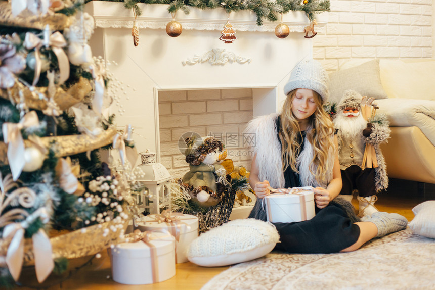 帽子十二月圣诞树下面的小女孩带礼物盒在装饰着客厅和传统火炉的地方童年图片