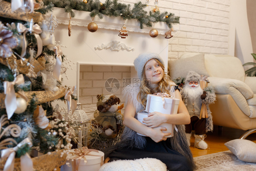 盒子圣诞节树下面的小女孩带礼物盒在装饰着客厅和传统火炉的地方壁图片