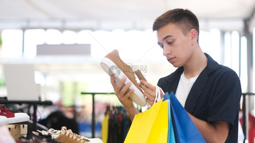 店铺喜悦青年男子在购物中心时选择鞋同子衣服图片