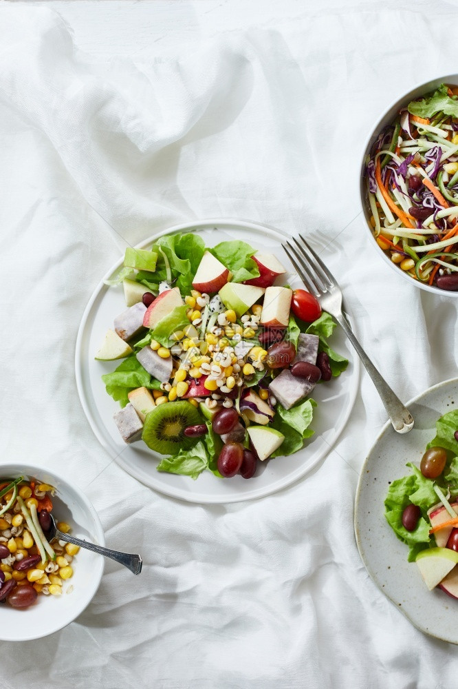 新鲜的开胃菜叶子美味水果沙拉和白桌上不同水果健康食品概念在白色桌子上图片