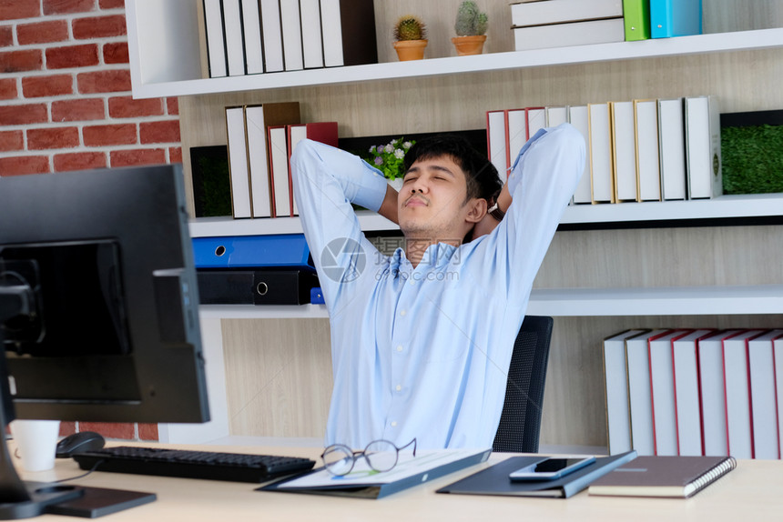 松弛坐着休息年轻的青亚洲人办公室男子在桌电脑室生活方式商业状况等工作时伸展身体以放松力图片