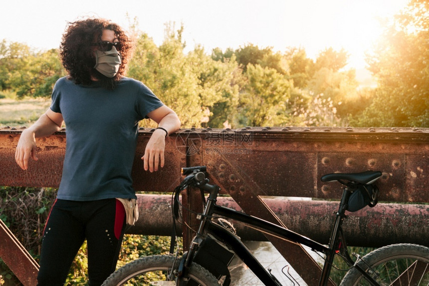 阳光男子在野外佩戴科面罩和骑自行车时在金属桥上用19号鱼群在西班牙的降级时身着脚踏单车疾病户外图片