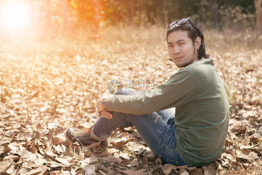 20多岁太阳年轻的亚洲男子坐在干叶上放松情绪户外图片