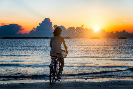 白种人女孩在日出时海中骑自行车冒险跑图片