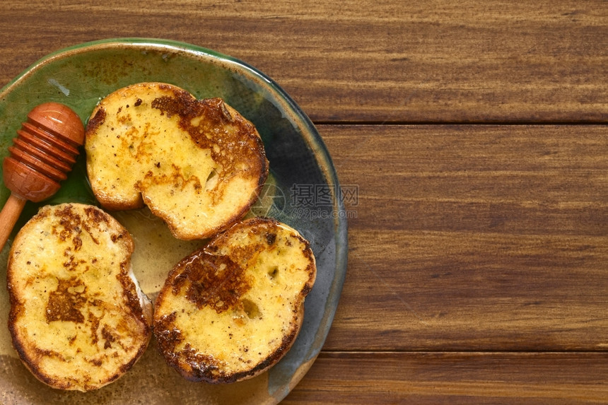 水平的西班牙语制作法式吐司由加蜂蜜的包面和制成侧边有蜂蜜薄饼用自然光照在黑木头上图片