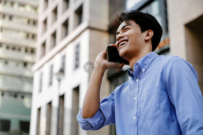 在城市中使用移动电话的年轻亚洲商人微笑城市中的移动电话数字城市阅读图片