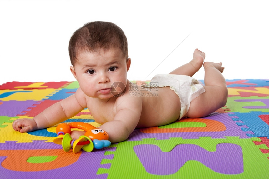 可爱的白人西班牙裔孩子躺在肚上一个多彩的加花地板砖上面有字母和一个玩具孤立无援软垫男瓷砖图片