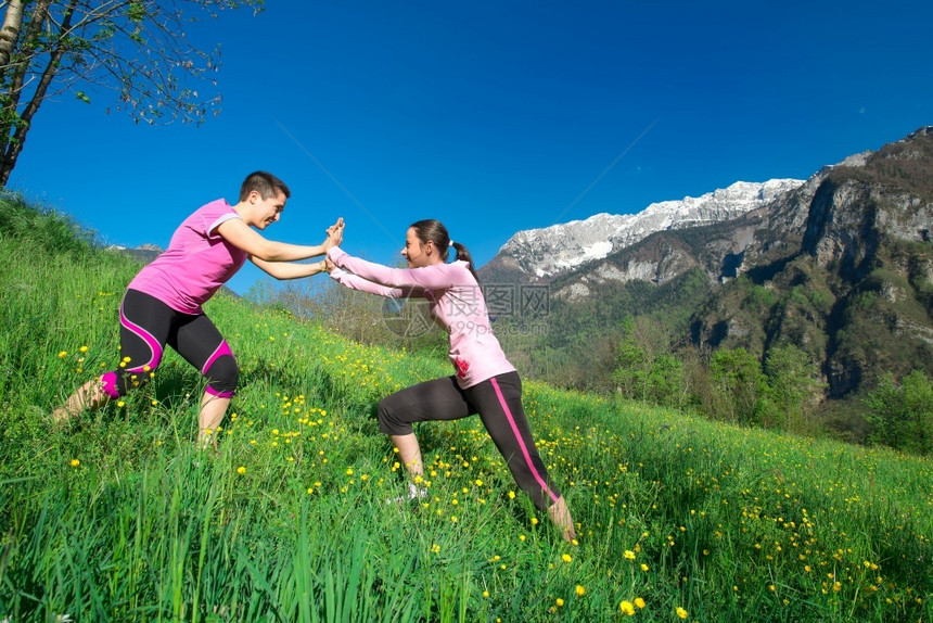 两个年轻的女孩在美丽一天草原上玩耍周围环绕着山地风景草乐趣爱图片
