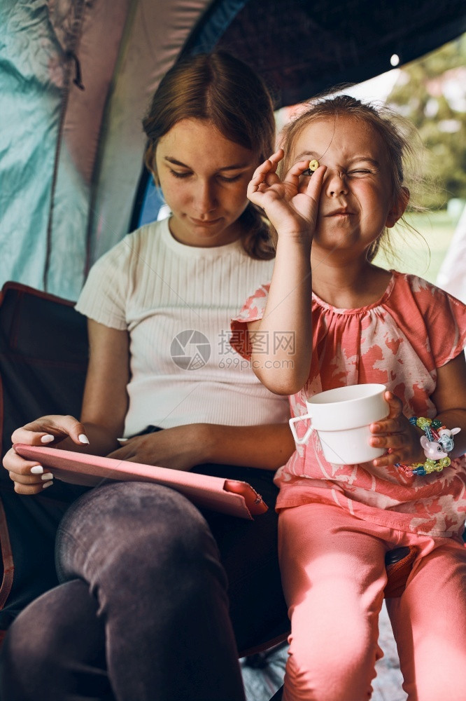 在暑假期间两个女孩姐妹在露营儿童帐篷中度过家庭时间她们利用平板电脑在网上玩游戏姐妹姊们在夏假期间用平板电脑在网上玩游戏露营儿童帐图片