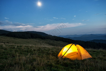 黄色的景观黑暗在黄昏山峰上红橙色帐篷从里面点燃天空月亮和星在黄昏的山峰上红橙色帐篷图片
