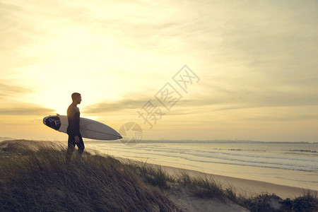 晴天成人一个在沙丘上冲浪的者仰望着海日落图片