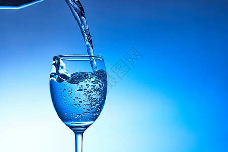将水倒入玻璃中以蓝底为的玻璃杯喝寒冷瓶子图片
