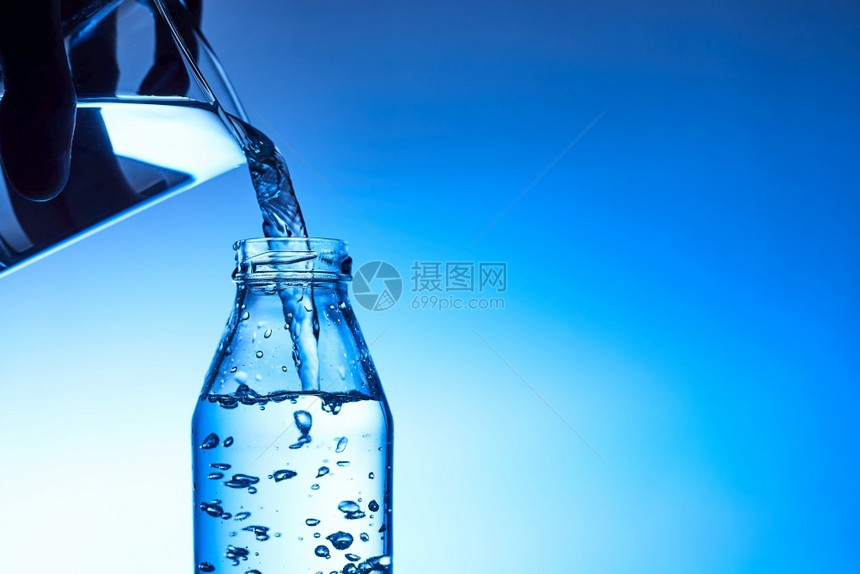 将水倒入玻璃中以蓝底为的玻璃杯饮料瓶子浇注图片