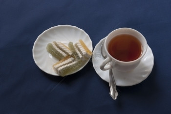 花喝喜碧须茶和一盘橘子酱汁茶以及一盘蓝布背景的彩色柑橘糖果图片