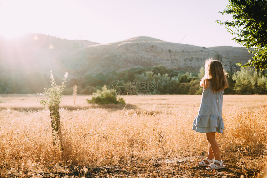 年轻的金发女孩在田野中玩阳光日落时身着背面有山丘的裙子微笑白种人图片