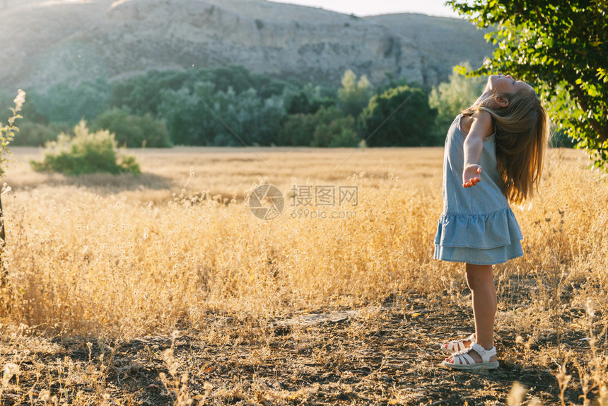 孩子可爱的户外金发年轻女孩在田野中玩阳光日落时身着背面有山丘的裙子图片