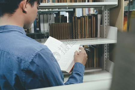 在书架前阅读的男学生图片