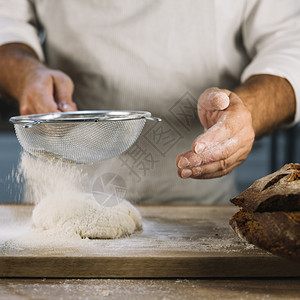 织物业务揉面包师通过钢筛子切碎面粉选图片