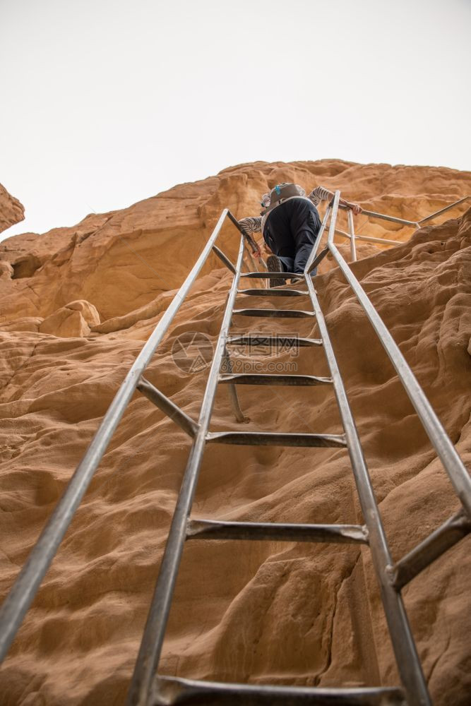 冒险结石形成以色列南部蒂姆纳公园拱门岩石上的女人爬梯子靠近艾尔塔蒂姆纳公园拱门的女人图片