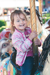 可爱笑的小女孩骑着马在游乐场环绕旋转木马喜悦孩子坦率图片